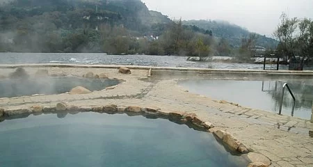 Termas naturales en un entorno montañoso en Galicia, con vapor y un río al fondo_351